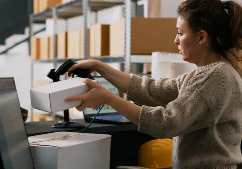 A woman managing inventory on a computer in a warehouse setting, illustrating real-time inventory tracking with wholesale distribution ERP software.