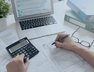 Person working with financial documents, calculator, and laptop, symbolizing analysis and comparison of ERP and accounting software solutions